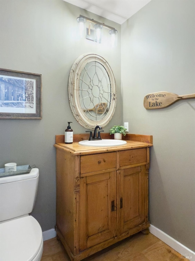 half bath with toilet, baseboards, and vanity