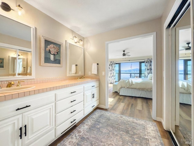 full bath with double vanity, ensuite bath, a sink, and wood finished floors