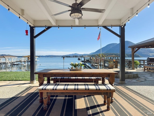 view of patio featuring a dock, a water and mountain view, a ceiling fan, and outdoor dining space