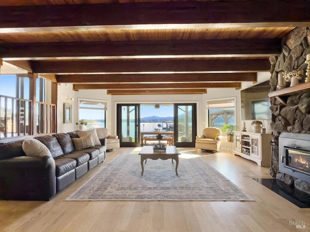 living area with wooden ceiling, beam ceiling, wood finished floors, and a stone fireplace