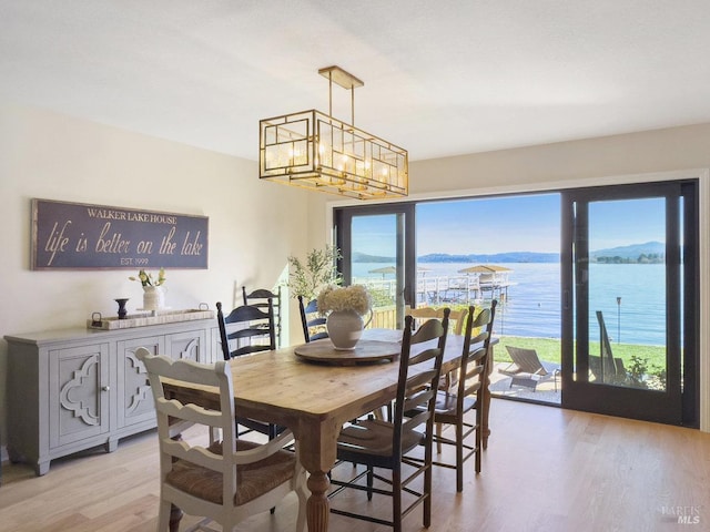 dining space with a water view, light wood finished floors, and an inviting chandelier