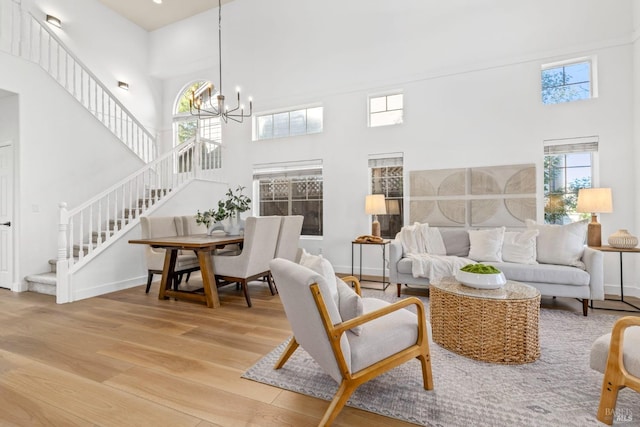 living area with a notable chandelier, a high ceiling, wood finished floors, baseboards, and stairway