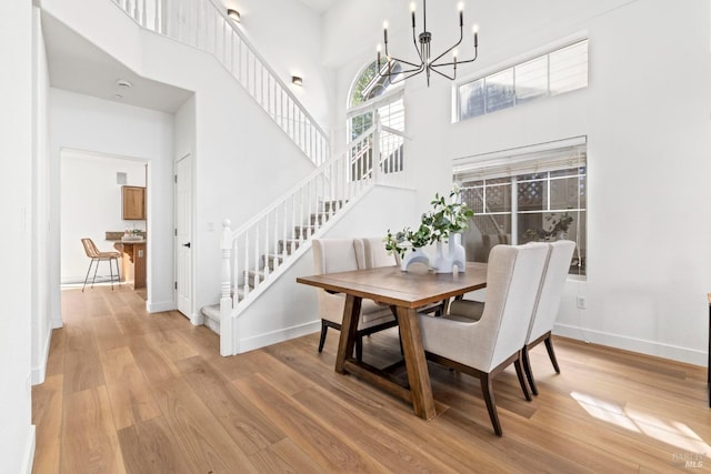 dining area with a notable chandelier, a towering ceiling, baseboards, stairs, and light wood finished floors