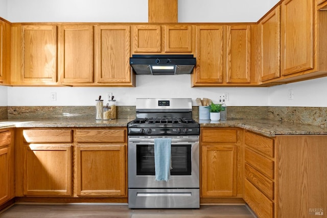 kitchen with stainless steel gas stove, dark stone counters, and under cabinet range hood