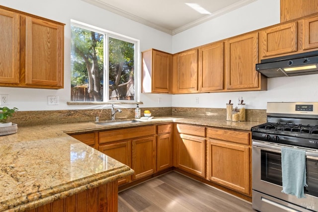 kitchen featuring under cabinet range hood, a sink, ornamental molding, brown cabinetry, and stainless steel range with gas stovetop