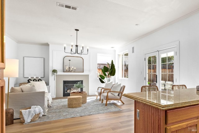 living room featuring visible vents, light wood-style floors, an inviting chandelier, a glass covered fireplace, and crown molding