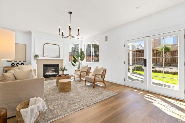 living room featuring a chandelier, ornamental molding, wood-type flooring, and a glass covered fireplace