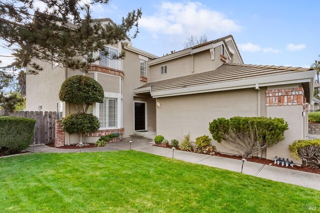 view of front of home with stucco siding, a tiled roof, fence, and a front lawn