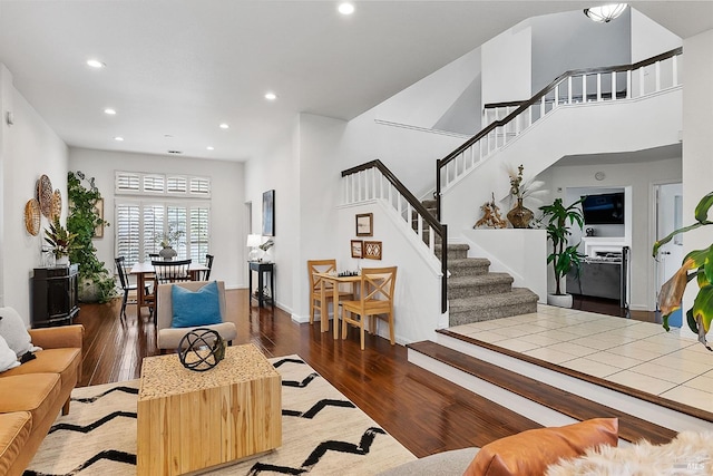 living area with baseboards, recessed lighting, stairway, a high ceiling, and wood finished floors