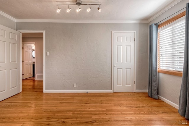 empty room with light wood finished floors, baseboards, ornamental molding, and a textured wall