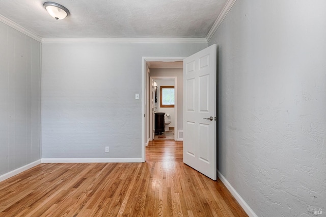 empty room with a textured ceiling, a textured wall, light wood-style flooring, baseboards, and ornamental molding