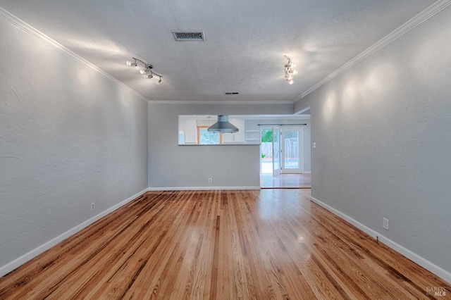 empty room featuring light wood-style floors, visible vents, and crown molding