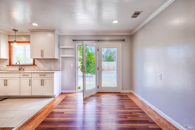 kitchen featuring a sink, visible vents, light wood-type flooring, backsplash, and crown molding