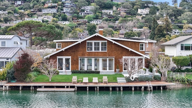 back of house featuring a water view, a chimney, and a lawn