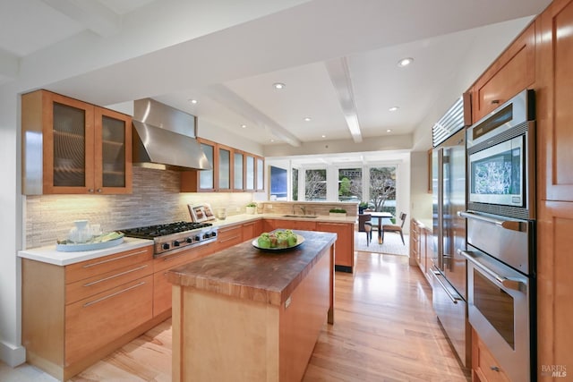 kitchen featuring wall chimney exhaust hood, butcher block countertops, beamed ceiling, a peninsula, and stainless steel gas cooktop