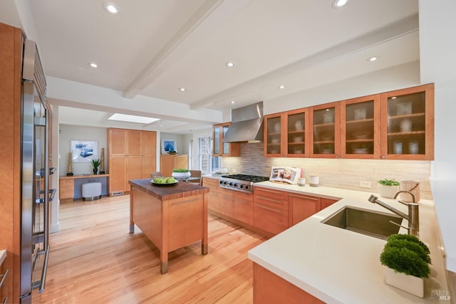 kitchen with beam ceiling, tasteful backsplash, appliances with stainless steel finishes, a sink, and wall chimney exhaust hood