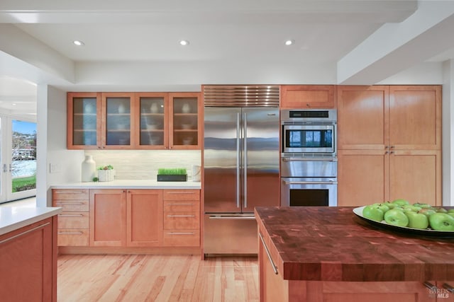 kitchen with recessed lighting, appliances with stainless steel finishes, light wood-type flooring, backsplash, and glass insert cabinets