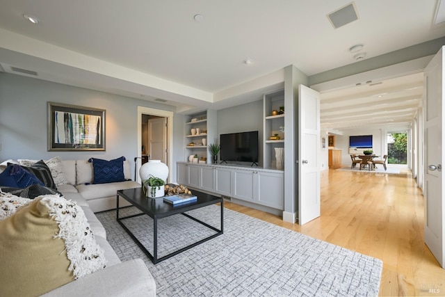 living room with light wood-style flooring, built in shelves, and visible vents