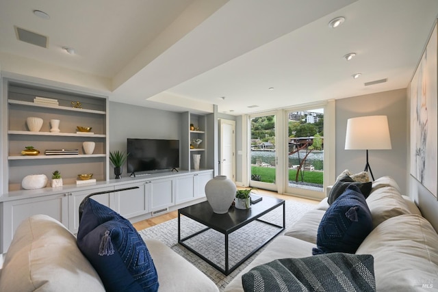 living room featuring light wood finished floors, built in shelves, and visible vents