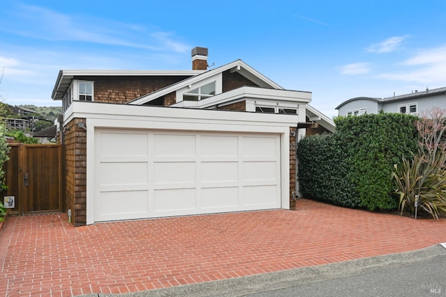 view of front of home featuring a garage, a chimney, fence, and decorative driveway