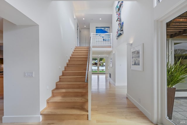 interior space featuring baseboards, a towering ceiling, wood finished floors, stairs, and recessed lighting