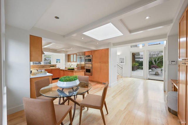 dining area with light wood-type flooring, a skylight, and beamed ceiling