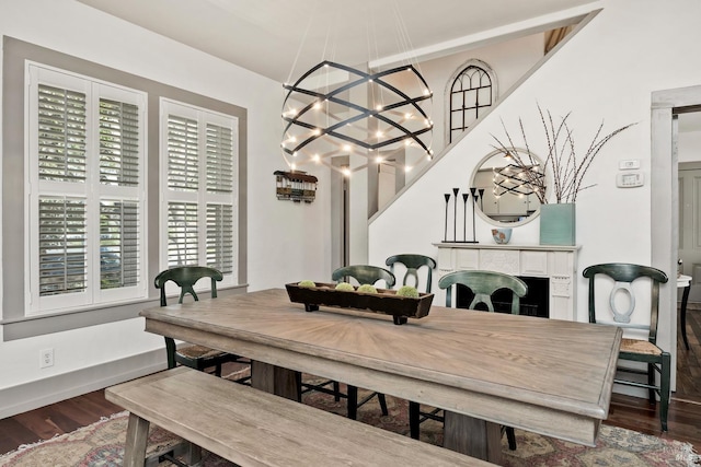 dining space featuring baseboards, a tile fireplace, wood finished floors, and a notable chandelier