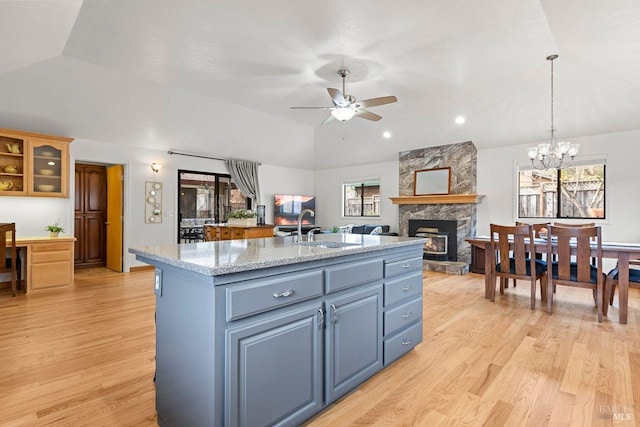 kitchen with vaulted ceiling, a kitchen island with sink, a sink, and light wood finished floors