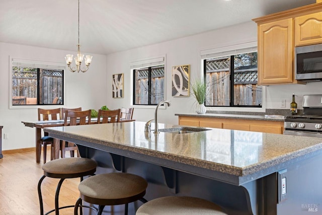 kitchen with appliances with stainless steel finishes, a kitchen breakfast bar, dark stone countertops, light brown cabinetry, and a sink