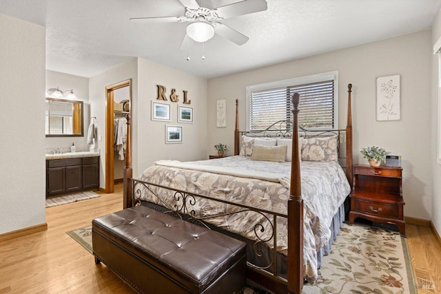 bedroom featuring a textured ceiling, a walk in closet, light wood-style flooring, and baseboards