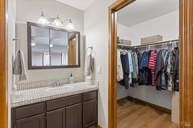 bathroom featuring a walk in closet, vanity, a textured ceiling, wood finished floors, and baseboards