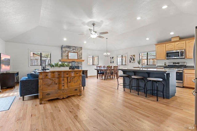 kitchen featuring stainless steel appliances, lofted ceiling, light wood finished floors, and a kitchen bar