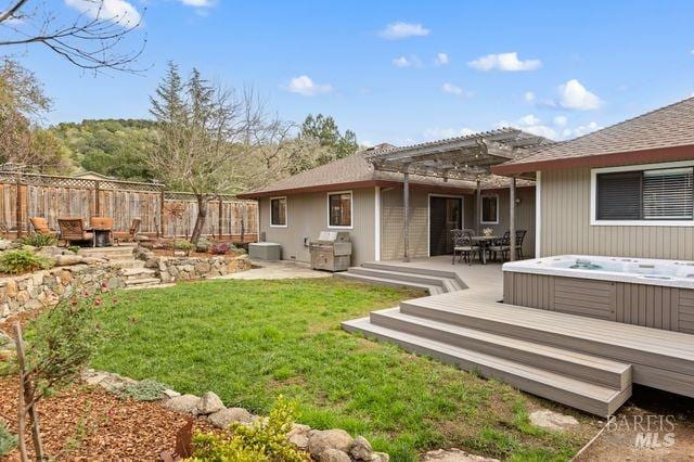 rear view of house with central air condition unit, an outdoor hot tub, a lawn, fence, and a pergola