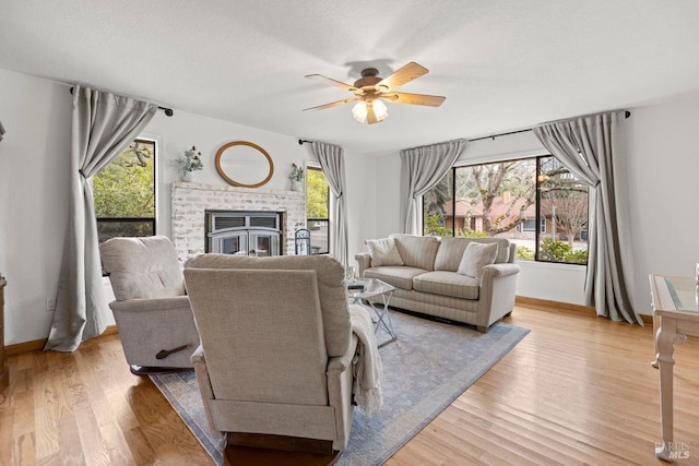 living room with a fireplace, ceiling fan, a textured ceiling, wood finished floors, and baseboards