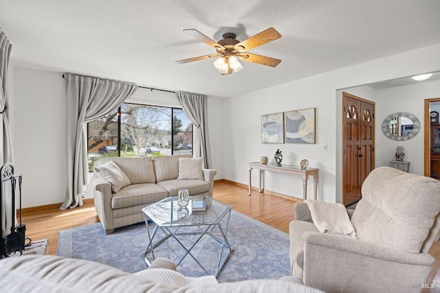 living room with ceiling fan, light wood finished floors, a textured ceiling, and baseboards