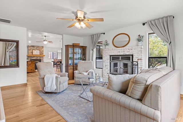 living room with a ceiling fan, visible vents, a stone fireplace, and wood finished floors