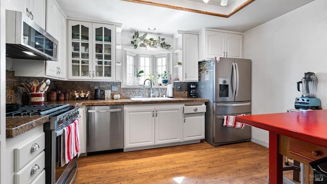 kitchen featuring a sink, white cabinets, appliances with stainless steel finishes, light wood finished floors, and dark countertops