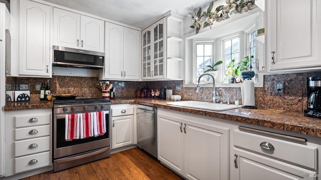 kitchen with a sink, white cabinetry, appliances with stainless steel finishes, dark wood finished floors, and glass insert cabinets