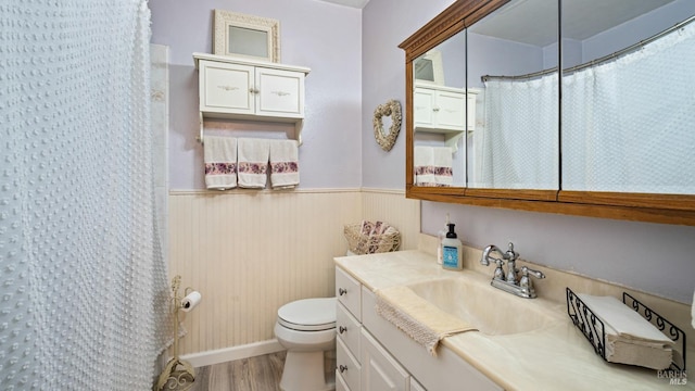 bathroom featuring curtained shower, toilet, wainscoting, vanity, and wood finished floors