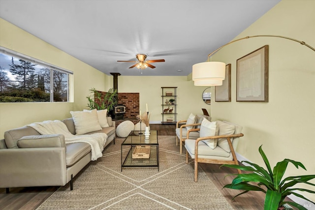 living room featuring a wood stove, ceiling fan, baseboards, and wood finished floors