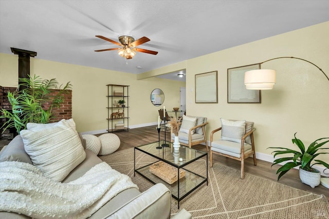 living area with ceiling fan, wood finished floors, a wood stove, and baseboards