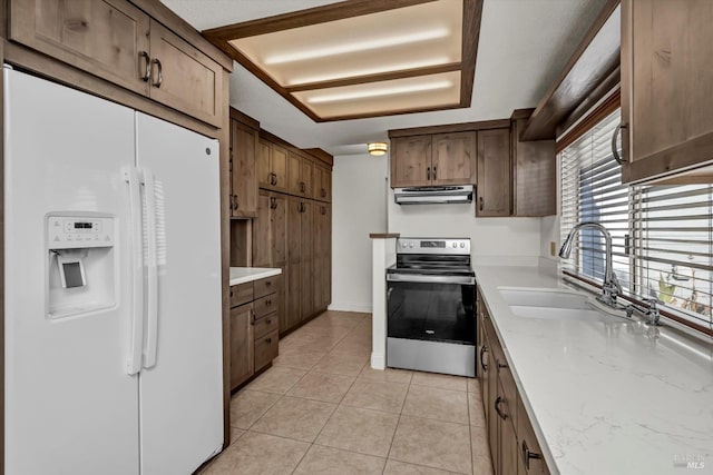 kitchen with light tile patterned floors, stainless steel electric range, under cabinet range hood, white fridge with ice dispenser, and a sink