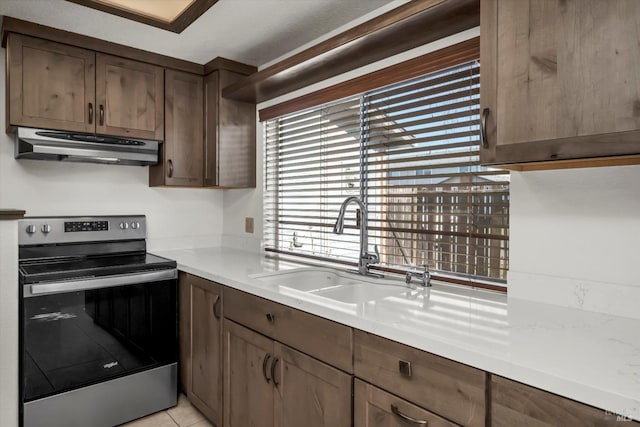 kitchen featuring light tile patterned floors, stainless steel electric stove, light countertops, a sink, and under cabinet range hood