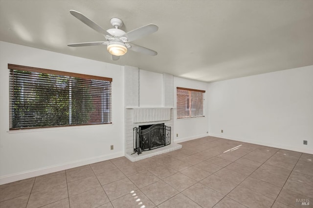 unfurnished living room featuring a brick fireplace, ceiling fan, light tile patterned floors, and baseboards