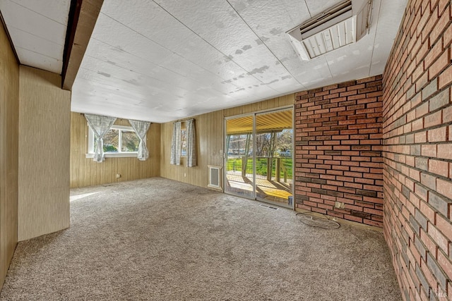 carpeted empty room featuring brick wall, wood walls, and visible vents