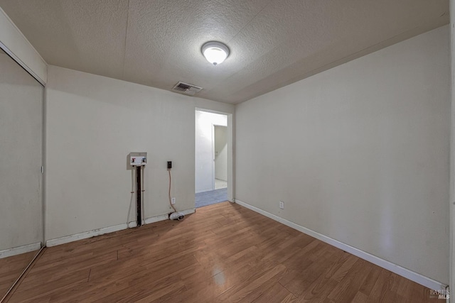 unfurnished room with a textured ceiling, wood finished floors, visible vents, and baseboards