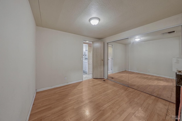 spare room with baseboards, visible vents, light wood-style flooring, and a textured ceiling