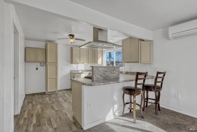 kitchen featuring light wood-style flooring, a kitchen breakfast bar, a wall mounted air conditioner, a peninsula, and island exhaust hood