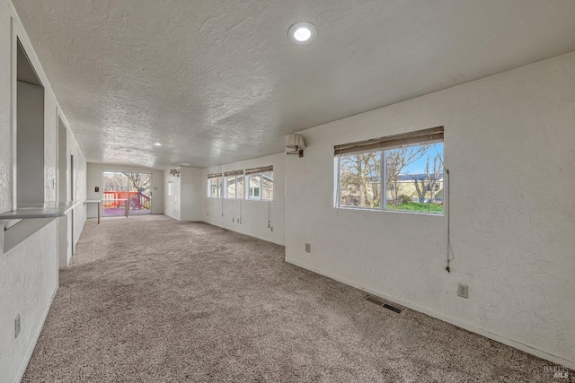 empty room with visible vents, a textured wall, light carpet, and a textured ceiling