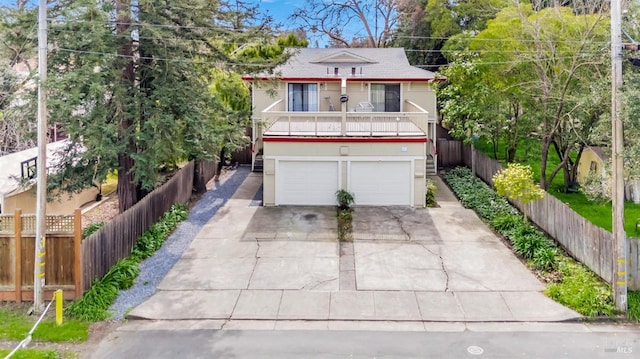 view of front of property featuring a garage, concrete driveway, fence, and a balcony